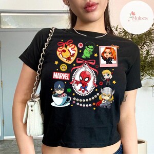 May include: Black cropped t-shirt with a colorful graphic print of various Marvel characters, including Iron Man, Spider-Man, Captain America, Hulk, Thor, and Black Widow. The text "MARVEL" and "SUPERHERO SQUAD" are also included in the design.