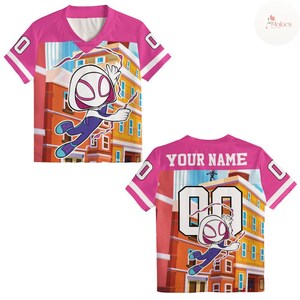 Puede incluir: Camiseta rosa y blanca de manga corta con un dibujo animado de superh&eacute;roe. La camiseta tiene el n&uacute;mero "00" en la espalda y "YOUR NAME" encima. Las mangas y el cuello est&aacute;n ribeteados en blanco.