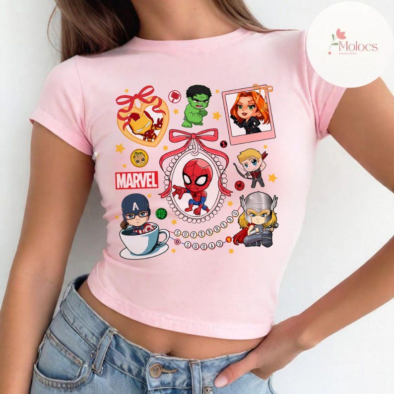 May include: Pink cropped t-shirt with a colorful graphic print of various Marvel superheroes, including Spider-Man, Hulk, Iron Man, Captain America, Black Widow, and Thor. The shirt also features the word "MARVEL" in a red and white font.