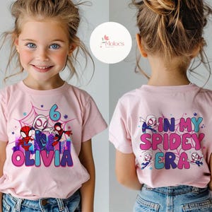 May include: Pink t-shirt with a graphic of Spider-Man characters and the text "Olivia" on the front. The back of the shirt has the text "In My Spidey Era" with Spider-Man characters.