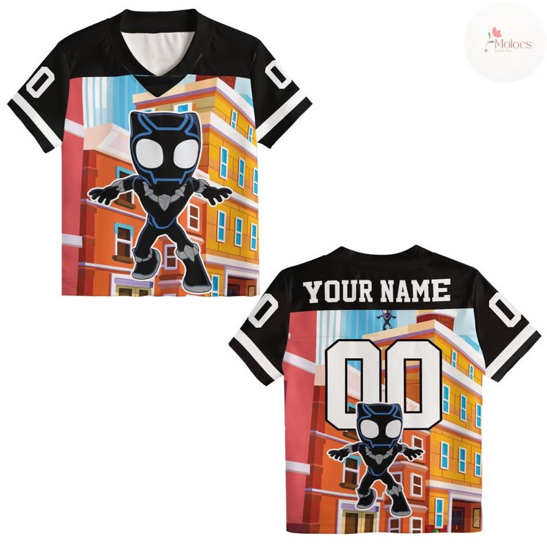 Puede incluir: Camiseta negra y blanca con un gr&aacute;fico de dibujos animados de un superh&eacute;roe frente a un edificio. La parte trasera de la camiseta tiene el texto "YOUR NAME" encima del n&uacute;mero "00". Las mangas son negras con detalles blancos.