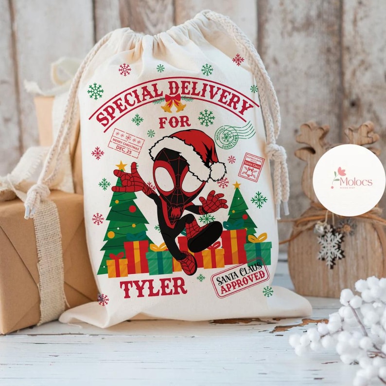 May include: A cream-colored drawstring gift bag with a festive design. The bag features the text "SPECIAL DELIVERY FOR TYLER" and a cartoon Spider-Man character wearing a Santa hat. Christmas trees, presents, and snowflakes decorate the bag.
