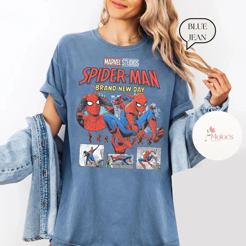 Op de afbeelding: Blauw T-shirt met een Marvel Studios Spider-Man-afbeelding. Het ontwerp bevat de woorden "Spider-Man Brand New Day" in rood en wit, en illustraties van de superheld. Het shirt heeft opgerolde mouwen.