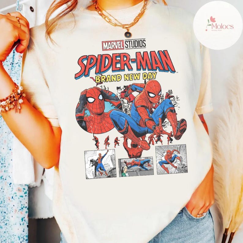 Op de afbeelding: Cr&egrave;mekleurig T-shirt met het Marvel Studios Spider-Man logo en de tekst "Brand New Day". De afbeelding toont Spider-Man in actieposes, met rode en blauwe kostuumdetails. Het shirt heeft korte mouwen.