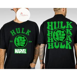 May include: Black t-shirts with a green Hulk graphic. The front of the shirt features the word "Hulk" above a green fist emblem, with "EST. 2014" and the Marvel logo. The back of the shirt repeats "Hulk" four times around a fist.