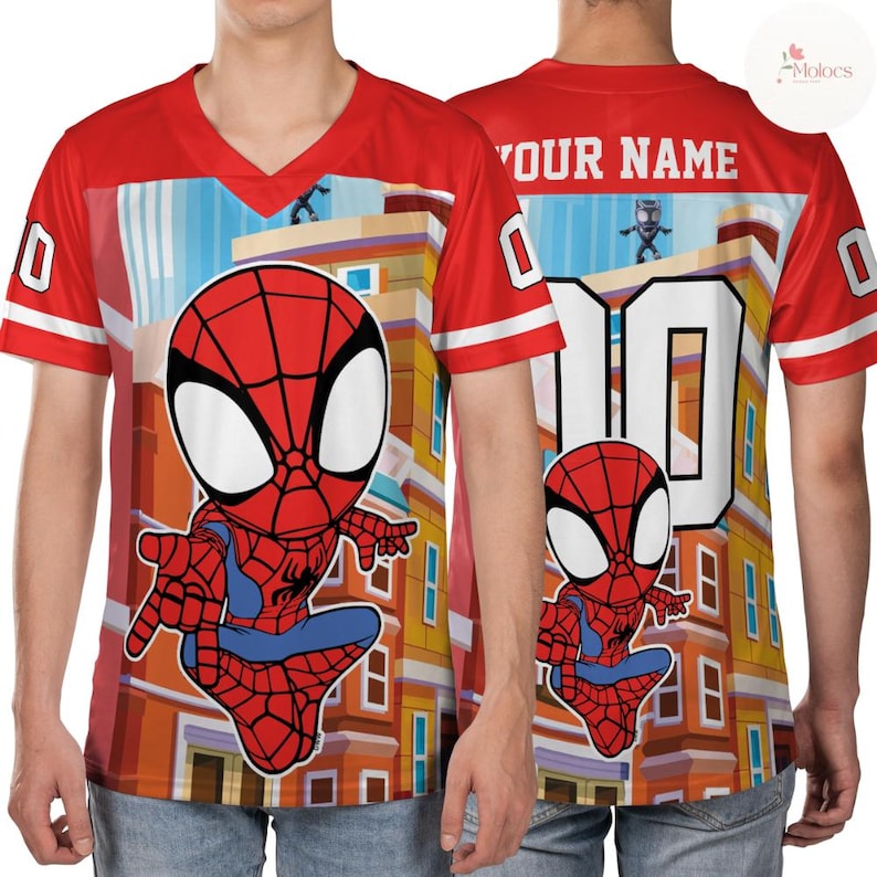 Puede incluir: Camiseta roja con cuello en V con un dise&ntilde;o de Spider-Man de dibujos animados en la parte delantera y trasera. La camiseta tiene rayas blancas en las mangas y el n&uacute;mero "10" en la espalda. El texto "YOUR NAME" est&aacute; encima del n&uacute;mero.