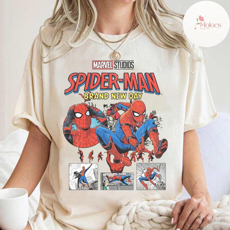 Op de afbeelding: Cr&egrave;mekleurig T-shirt met een afbeelding van Spider-Man in actieposes. Het ontwerp bevat de tekst "MARVEL STUDIOS SPIDER-MAN BRAND NEW DAY" in rood, blauw en geel. Het shirt heeft korte mouwen en een ronde hals.