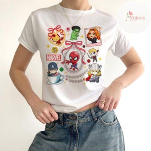 May include: White t-shirt with a colorful cartoon design featuring various Marvel characters, including Spider-Man, Iron Man, Captain America, Hulk, Thor, and Black Widow. The design includes the word "MARVEL" in a red and yellow font.