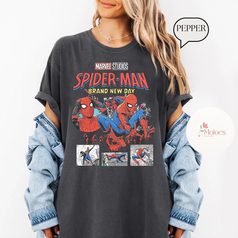 Op de afbeelding: Donkergrijs t-shirt met een Marvel Studios Spider-Man graphic. Het ontwerp bevat de woorden "Spider-Man Brand New Day" en illustraties van de superheld. Het t-shirt wordt door een persoon gedragen.
