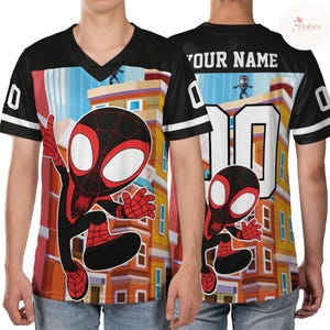 Puede incluir: Camiseta negra y blanca con cuello en V con un gr&aacute;fico de dibujos animados de Spider-Man en la parte delantera y trasera. La camiseta presenta el n&uacute;mero 0 y las palabras "YOUR NAME" en la espalda. El fondo muestra un paisaje urbano.