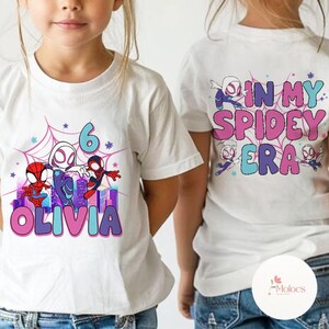 May include: Two white t-shirts with a Spider-Man theme. One shirt has a graphic of Spider-Man characters and the text "Olivia" and "6". The other shirt has the text "In My Spidey Era".
