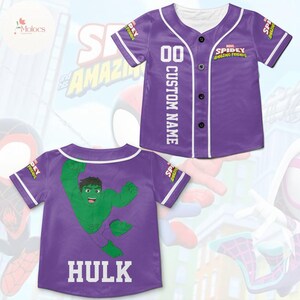 May include: Purple baseball jersey with a white trim and buttons. The front of the jersey has the text "SPIDEY AMAZING FRIENDS" and the number "00" with the text "CUSTOM NAME" below. The back of the jersey has a green cartoon image of the Hulk and the text "HULK" below.