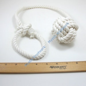 May include: White cotton rope tied into a large knot, with a smaller loop knot at the other end. The rope is about 8 inches long.