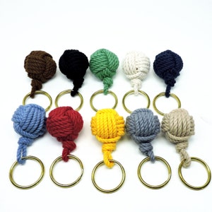 May include: Ten colorful rope keychains with gold key rings. The keychains are made of knotted rope and come in a variety of colors, including red, blue, green, yellow, brown, black, and white.