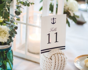 May include: White table number card with a navy blue anchor and the text "Table 11". The card is attached to a white rope knot.
