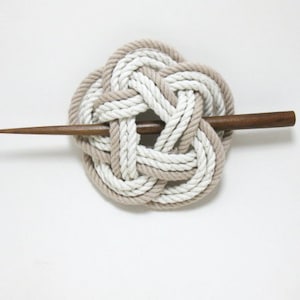 May include: A white and brown rope hair clip with a wooden stick. The rope is tied in a knot and the stick is inserted through the center of the knot.