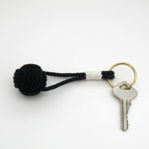 May include: Black and white rope keychain with a knot at the end and a brass key ring. A silver key is attached to the ring.