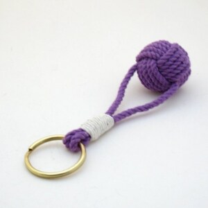 May include: Purple rope keychain with a white accent and a brass key ring.