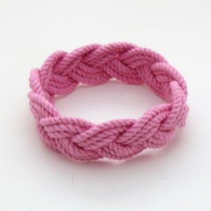 May include: A pink braided rope bracelet. The rope is woven into a circular shape, creating a simple and stylish accessory.