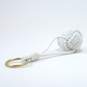 May include: White rope keychain with a knotted ball and a gold metal ring.