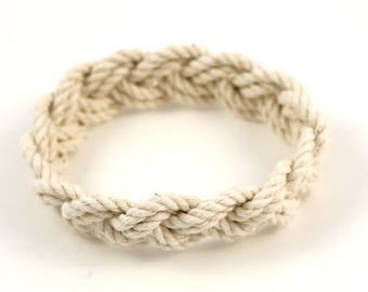 May include: A white rope bracelet with a braided design. The bracelet is made of natural cotton rope and is a simple, yet stylish accessory.