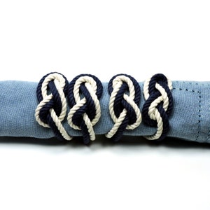 May include: Four navy blue and white rope napkin rings tied together on a blue napkin. The rings are made of a thick rope with a knot design.