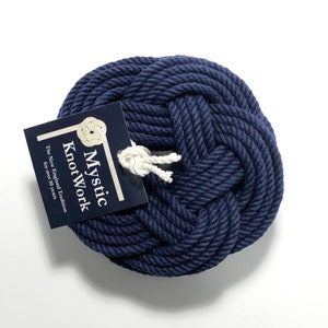 May include: A navy blue rope coaster with a knot design. The coaster has a tag attached that says "Mystic KnotWork The New England Tradition for over 50 years."