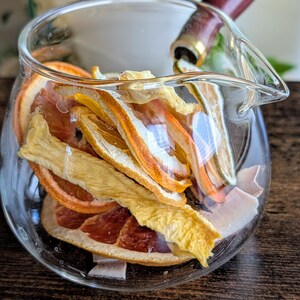 Peut inclure: Une carafe en verre remplie de tranches d'orange et de pamplemousse séchées, et de lanières de mangue séchées.