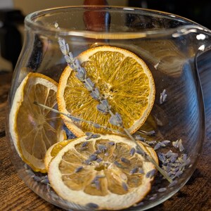 May include: A glass jug filled with dried orange slices and lavender flowers. The jug is sitting on a wooden table.