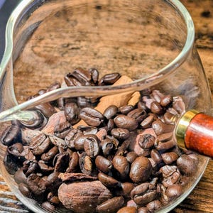 Peut inclure: Une carafe en verre remplie de grains de café torréfiés et de morceaux de bâton de cannelle. La carafe est posée sur une surface en bois.