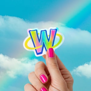 May include: A holographic sticker in the shape of the letter "W" with a rainbow gradient and a yellow swirl. The sticker is held up against a blue sky with clouds and a rainbow.