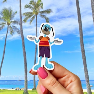 May include: A die-cut sticker featuring a cartoon dog with blue fur, wearing an orange and red striped shirt, purple shorts, and brown sleeves. The dog has its arms out, with a beach and palm trees in the background.