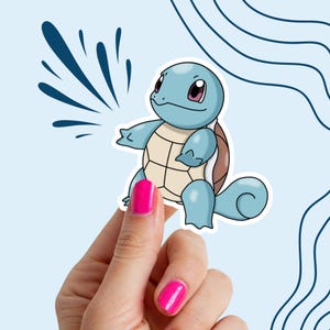 May include: A blue and brown cartoon turtle sticker with a white outline. The sticker is being held by a hand with pink nail polish.
