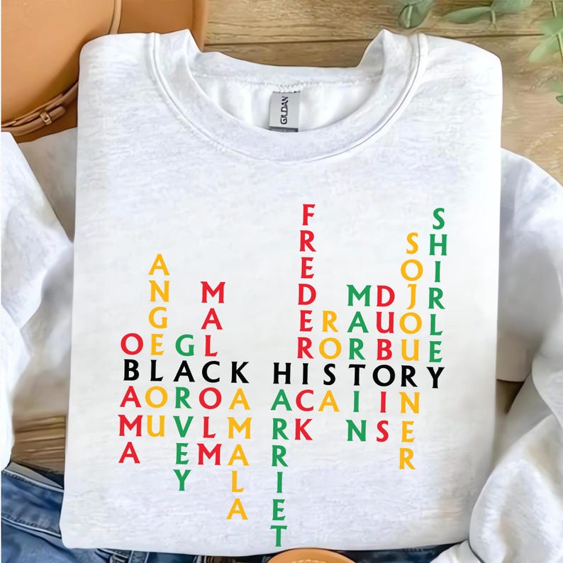 May include: White sweatshirt with the words "BLACK HISTORY" in black, and other names in red, green, yellow, and black. The sweatshirt has a crew neck and the brand name "GILDAN" is visible on the collar.
