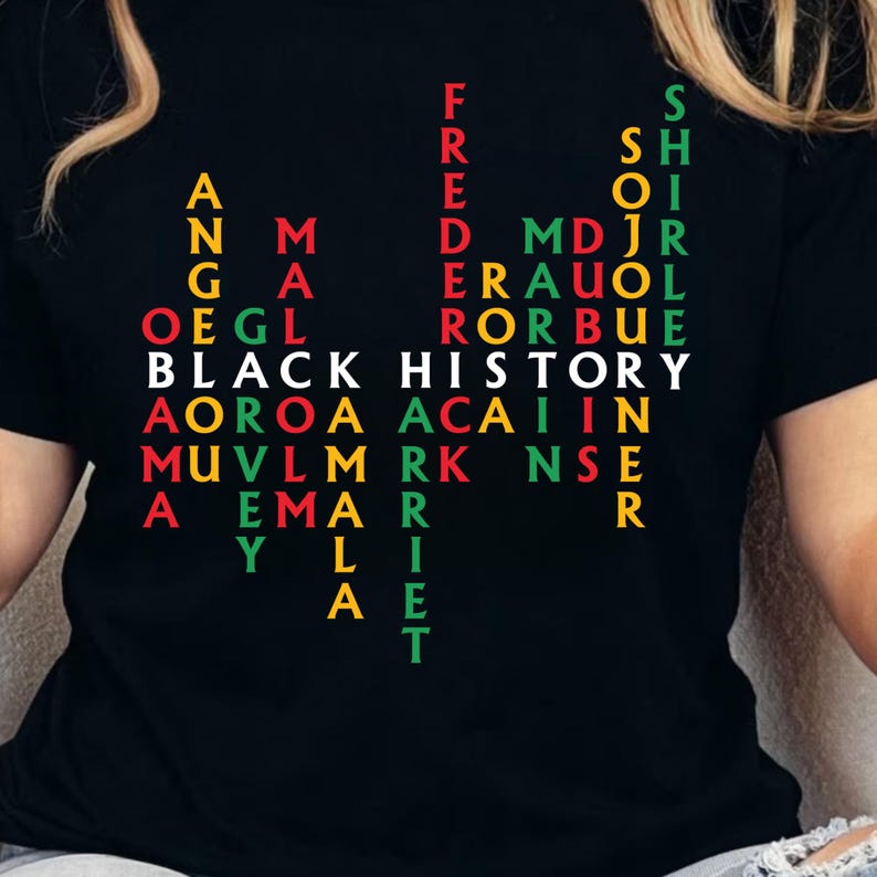 May include: Black t-shirt with a colorful text design that reads "BLACK HISTORY" in white, with other words and names in red, green, and yellow. The shirt features a unique, artistic arrangement of letters and words.