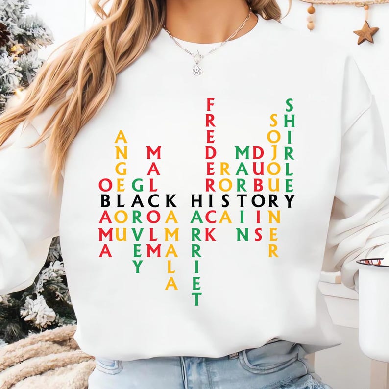 May include: White sweatshirt with the words "BLACK HISTORY" in black, and other names in various colors. The names are arranged vertically and horizontally. The sweatshirt is a crew neck style.