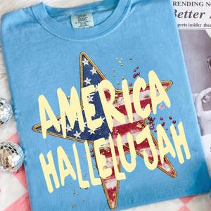 Pu&ograve; includere: T-shirt Comfort Colors azzurra con un design a stella con il motivo della bandiera americana e le parole "AMERICA HALLELUJAH" in giallo. La stella &egrave; bordata d'oro, con macchie dorate. La maglietta ha un girocollo.