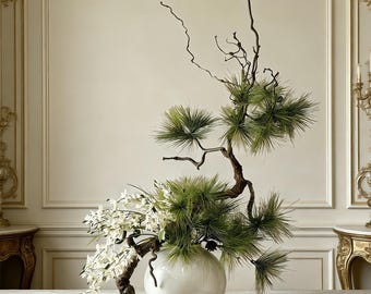 May include: A white spherical ceramic vase containing an arrangement of green pine branches and white orchid flowers. The arrangement features a curved, textured brown branch extending to the left, with pine needles and white blossoms attached.