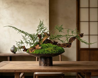 May include: A dark metal pedestal bowl filled with vibrant green moss, textured driftwood, and delicate fern fronds. The arrangement is centered in a wide, shallow vessel with a cylindrical base, showcasing a natural composition of organic elements.