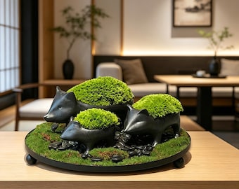 May include: A set of three black animal-shaped planters on a round tray, each containing bright green moss. The planters are arranged on a bed of green moss and small black stones, creating a cohesive display of dark ceramic and vibrant greenery.