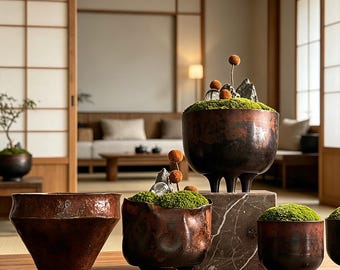 May include: A collection of dark, hammered copper-toned vessels with three legs, some containing vibrant green moss, small grey rock formations, and tiny orange spherical accents. The containers vary in shape, including wide bowls and deep pots.