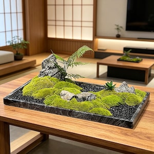 May include: A rectangular black marble tray containing a moss garden arrangement. The display features vibrant green moss mounds, several grey textured rocks, a small green fern, and a small succulent, all set against black gravel.