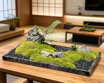 May include: A rectangular black marble tray containing a moss garden arrangement. The display features vibrant green moss mounds, several grey textured rocks, a small green fern, and a small succulent, all set against black gravel.