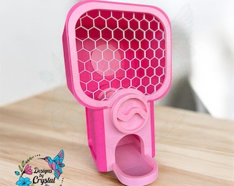 May include: A pink gumball machine with a honeycomb design on the front. The machine has a curved top and a dispensing tray at the bottom. The design includes the text "Designs by Crystal llc" with a hummingbird and floral graphic.