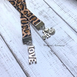 Puede incluir: Marcapáginas de cinta de estampado de leopardo con dos abalorios plateados. Un abalorio dice "I love my" y el otro abalorio dice "LOVE".