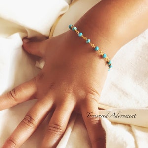 May include: A gold chain bracelet with turquoise beads. The bracelet is on a child's wrist.
