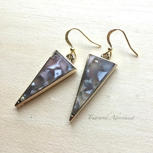 May include: A pair of gold triangle earrings with a gray and white marbled design. The earrings have a simple hook closure.