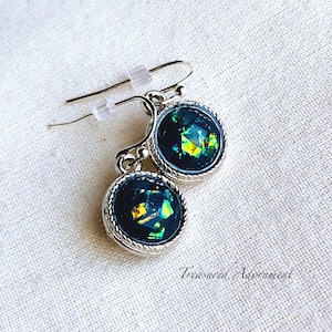 May include: A pair of silver earrings with green and black iridescent glass stones. The earrings have a simple design with a round stone set in a silver bezel.