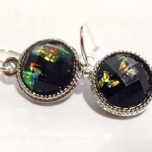Puede incluir: Un par de pendientes de plata con piedras redondas de vidrio negro iridiscente. Las piedras tienen un brillo iridiscente verde, dorado y azul.