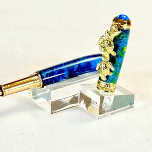The Sea Turtle Roller Ball pen features a stunning blue-ocean synthetic Fire Opal, turtle shell texture, and sea turtle clip. Truly a turtle lover gift. It comes either as a Rollerball or Fountain Pen. The cap posts securely with wide threads that won't cross. Hawaiian Honu Pen that has beautiful ocean themed features. One of my favorite Sea Creatures is the Sea Turtle. This Pen has it all. The pen comes with a windowed pen box making this item gift-ready.